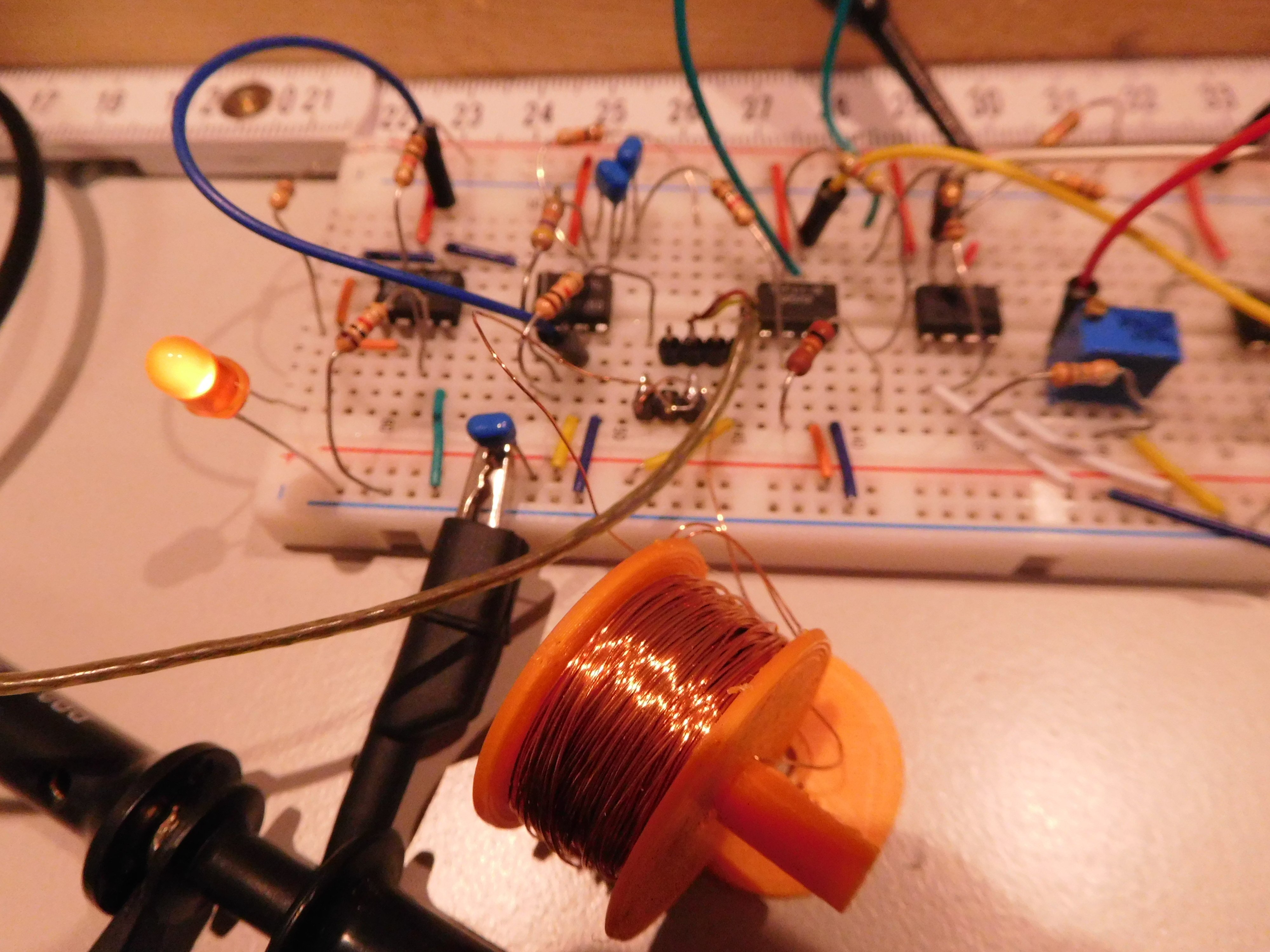 Verstärkerelektronik mit Kompensationsspule im Vordergrund; das Pick-Up-Signal kommt über die abgeschirmte Leitung (braun) rein; Die ICs von links nach rechts: 1 x LF357 für virtuelle Masse, 1 x OP07 für erste Verstärkerstufe (50) , 1 x OP07 für zweite Stufe (60) , 1 x Komparator LM311